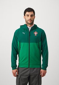 Zaļš sporta jakas ar rāvējslēdzēju priekšā, kapuci un Portugāles emblēmu. Izgatavota no gluda auduma, ar melniem rāvējslēdzējiem un Puma logotipu uz krūtīm.