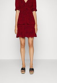 Rotes Kleid mit schwarzem Leopardenmuster, V-Ausschnitt, kurzen Puffärmeln, geschichtetem Design und schwingendem Saum. Kombiniert mit schwarzen Plateausandalen.