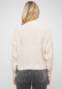 Chunky knit cream sweater with a high collar, ribbed texture, and drop shoulders. Cropped design with a straight hem and open weave pattern.