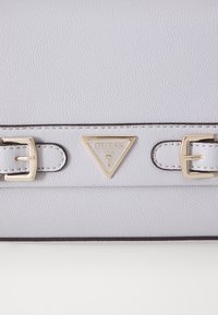 Light grey textured handbag with gold hardware, featuring a triangular logo and buckle accents, designed with a smooth finish and contrast stitching.