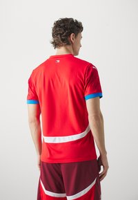 Rød atletisk trøje med blå accenter, der har et tjekkisk flagpatch, hvide striber og korteærmer. Lavet af letvægts, åndbart stof.