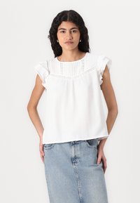Hvit bomullbluse med volangerm, plisségfront og blondekant. Kombinert med lys blå denimskjørt, brukt på en uformell måte.
