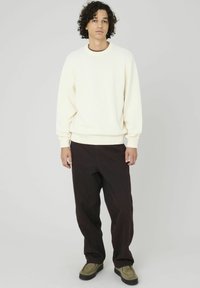 Sweatshirt en polaire de couleur crème avec des poignets et un ourlet côtelés, associé à un pantalon large marron foncé et des chaussures vert olive.