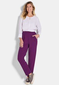 Witte blouse met een keyhole halslijn, gecombineerd met paars, hooggeformatteerde broeken met plooien en zijzakken. Metallic sneakers maken de look compleet.