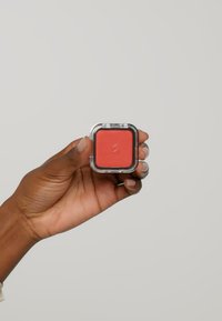 Compacto de rubor cuadrado en una caja de plástico transparente, con un vibrante polvo en color rojo coral. El compacto tiene un borde metálico plateado.