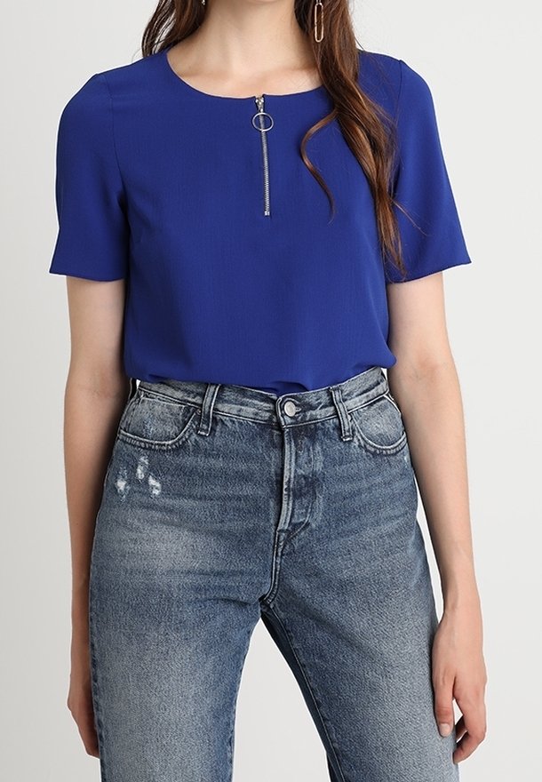 Modrá krátkosrstá blůza s kulatým výstřihem a předním kovovým zipem, spárovaná s vysokým pasem, roztrhanými džíny v světle modré barvě.