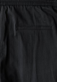 Black fabric shorts showcasing a smooth texture, elastic waistband, and a rear pocket with a stitched border. Simple and functional design.