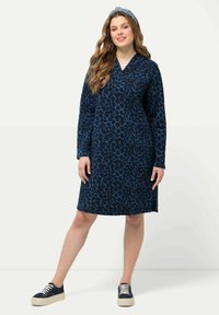 Marineblaues Kleid mit Leopardenmuster, langen Ärmeln und V-Ausschnitt. Kombiniert mit marineblauen Sneakers und einem passenden Haarband.