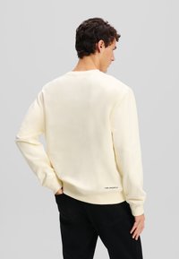Crème-kleurig sweatshirt gemaakt van zachte stof. Heeft een ronde halslijn, lange mouwen en een klein logo aan de achterkant van de zoom.