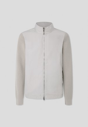 Chaqueta gris claro con un cuerpo suave y mangas de punto texturizadas, con un cuello alto y cremallera frontal. Diseño minimalista, material ligero.