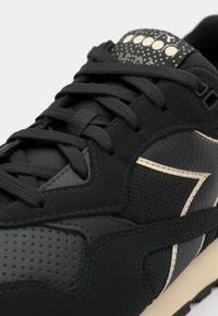 Black athletic sneaker featuring textured materials, a patterned tongue, and cream-colored accents. Laced with flat black shoelaces.