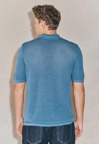 Hellblaues, gestricktes Poloshirt mit strukturierter Oberfläche, kurzen Ärmeln und klassischem Kragen, kombiniert mit dunklen Jeans.