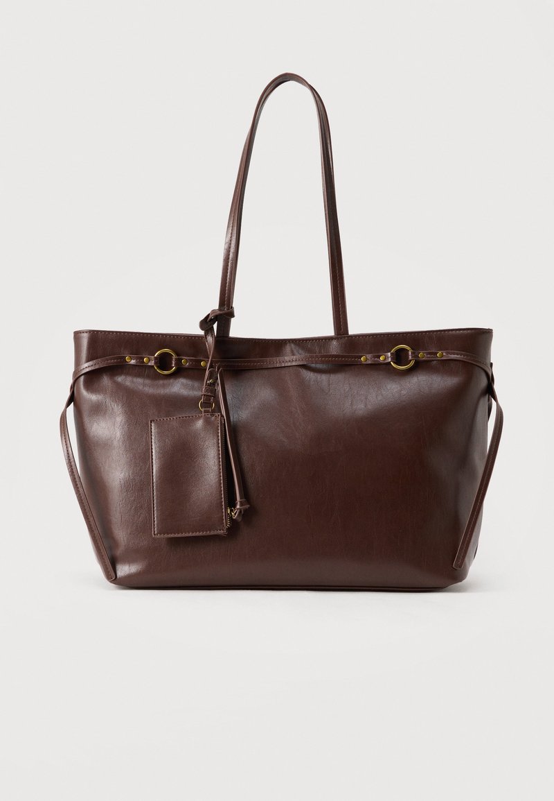 Sac cabas en cuir marron foncé avec deux longues anses, anneaux décoratifs en or, et pochette rectangulaire attachée avec fermeture éclair.