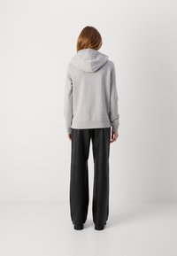 Grauer Hoodie mit einer Kordelzugkapuze, gerippten Bündchen und Saum, kombiniert mit hochgeschnittenen schwarzen Kunstlederhosen. Minimalistisches Design.