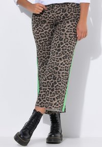 Luipaardprint jeans met groene zijkanten, voorzien van een relaxte pasvorm, een gefranjeerde zoom en gecombineerd met zwarte veterschoenen op een platform.