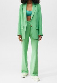 Groene linnen pak met een enkel knoop blazer, wijde broekspijpen en een cropped ribben tanktop. Beschikt over voorzakken en een gestructureerde stof.