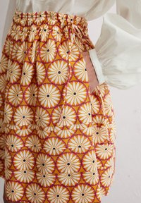 Bunte, gemusterte Röcke mit einem sich wiederholenden Blumenmuster in Orange, Weiß und Schwarz, ausgestattet mit einem elastischen Bund und Taschen.