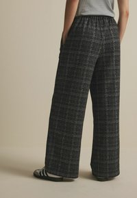 Pantalon à jambes larges en tissu texturé noir et blanc, doté d'une taille élastique, de poches latérales et d'un motif à carreaux.