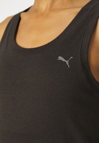 Zwart mouwloos tanktopje, gemaakt van zachte stof, met een subtiel grijs Puma-logo op de linkerborst, en een ronde halslijn.