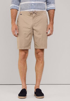 Shorts de bain beige avec un cordon de serrage à la taille, des poches latérales et une coupe droite, associés à des chaussures noires à enfiler. Tissu texturé.