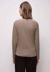 Długi rękaw, prążkowany top w kolorze taupe, o luźnym kroju i okrągłym dekolcie. Tkanina jest gładka z subtelną fakturą.