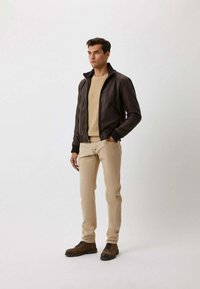 Bruine leren bomberjack met geribbelde boorden, gecombineerd met een beige sweater en beige slim-fit broek. Bruine veterschoenen maken de outfit compleet.