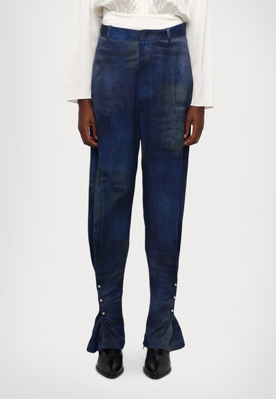 Pantalones de mezclilla en azul oscuro con un patrón texturizado, que presentan un fondo acampanado y detalles de botones a presión a lo largo del dobladillo.