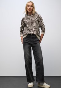 Hoodie met een bruin en beige zebrapatroon, gecombineerd met hoge zwarte denim jeans en witte sneakers.