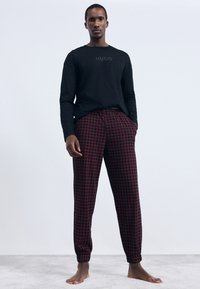 Schwarzes Langarmshirt mit geprägt "HUGO" Logo, kombiniert mit rot-schwarz karierten Hosen, die Seitentaschen und elastische Bündchen besitzen.