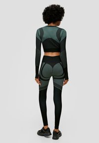 Zweiteiliges Sportoutfit in Dunkelgrün und Schwarz. Mit langen Ärmeln, geripptem Material und geschichteter Gestaltung mit kontrastierenden Mustern.