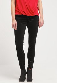 Černé slim-fit kalhoty vyrobené z měkké, strukturované tkaniny. Mají nízký pas a mírně elastický materiál pro pohodlí. V kombinaci s černými kotníkovými botami.