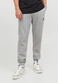 Gray sweatshirt pants with a relaxed fit, featuring a small black logo, elastic cuffs, and side pockets, paired with white and gray sneakers.
