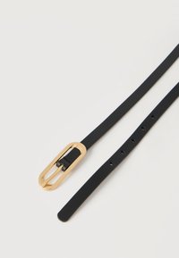 Ceinture en cuir noir avec boucle ovale en or et plusieurs trous d'ajustement, posée à plat sur une surface blanche.