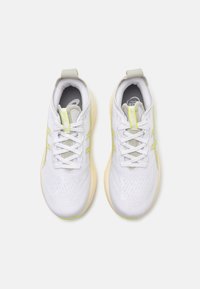 White athletic shoes with a textured upper, light gray accents, and neon green detailing on the sides. Features traditional lacing and a cushioned sole.