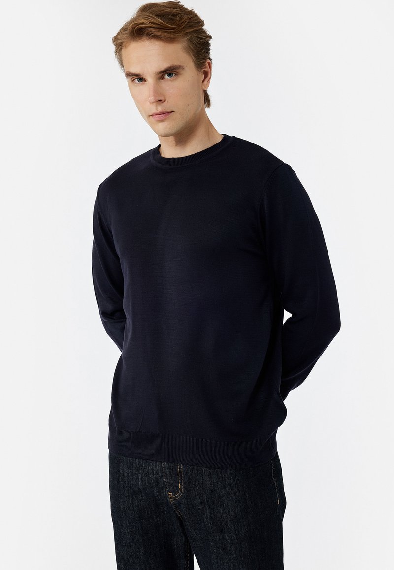 Marineblau gestrickter Pullover mit langen Ärmeln und Rundhalsausschnitt, der eine glatte Textur und Rippstrickabschlüsse an den Bündchen und am Saum aufweist.