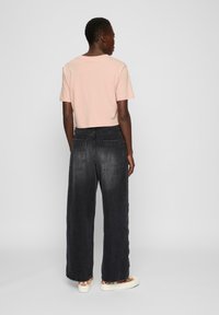 Kuttet lys rosa t-skjorte paret med vide mørkegrå jeans med baklommer og en logopatch nær midjen. Enkel design.