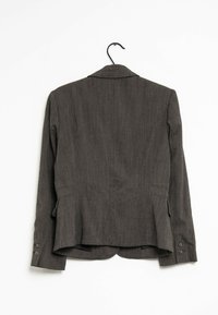 Šedý upravený blazer s texturovaným povrchem, obsahující jeden zadní rozparek, dvě vnější kapsy a manžety na knoflíky. Visí na černém háčku.