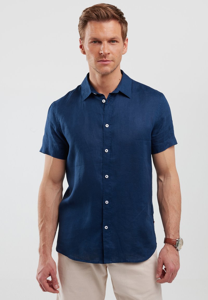 Camicia di lino azzurra a maniche corte con chiusura a bottoni, colletto a punta e cinque bottoni bianchi. Tessuto liscio con vestibilità comoda.