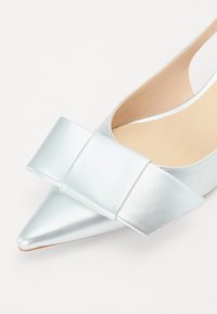 Chaussure argentée à bout pointu en cuir métallisé avec un large nœud décoratif sur le cou-de-pied et un design élégant et minimaliste. Texture lisse avec un intérieur beige.