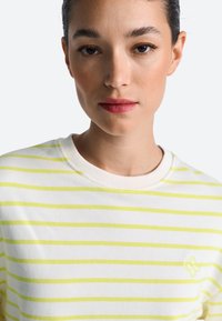 Weißes Baumwoll-T-Shirt mit gelben horizontalen Streifen, rundem Ausschnitt und einem kleinen Logo-Akzent auf der linken Brust. Glatte Textur.