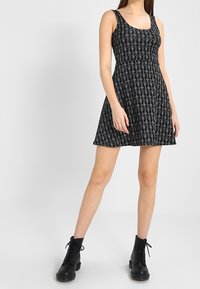 Černé bezramínkové šaty s přiléhavým tělem a rozšířenou sukní, s texturovaným vzorem. Nosené s černými šněrovacími botami.