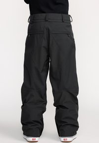 Pantalons de neige noirs avec une coupe ample, fabriqués en matériau durable. Les caractéristiques incluent des poches arrières et des coutures renforcées pour une meilleure mobilité.