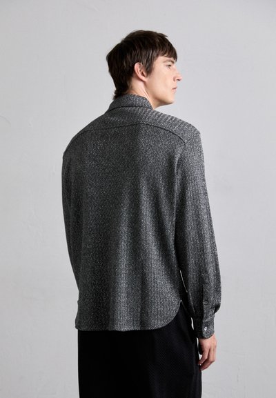 Camisa de manga larga en patrón de espiga en negro y gris, con cuello, puños abotonados y dobladillo redondeado. Tejido suave y texturizado.