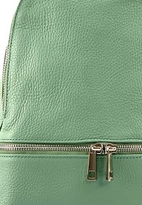 Sac à dos en cuir texturé vert avec une poche zippée à l'avant, mettant en valeur des éléments en métal argenté et une fermeture éclair lisse.