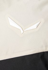 Beige textiel met een zwarte sectie eronder, met witte hoekige accenten die lijken op een logo of een designelement.