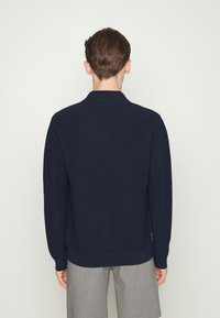 Námořnický pletený kardigan s vroubkovaným vzorem, s překládaným límcem, dlouhými rukávy a přiléhavým lemem. Viditelná struktura a čisté linie bez ozdob.