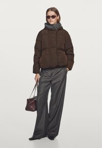 Brun puffet jakke med hætte og quiltet design, kombineret med grå viddebukser og en bordeaux håndtaske.