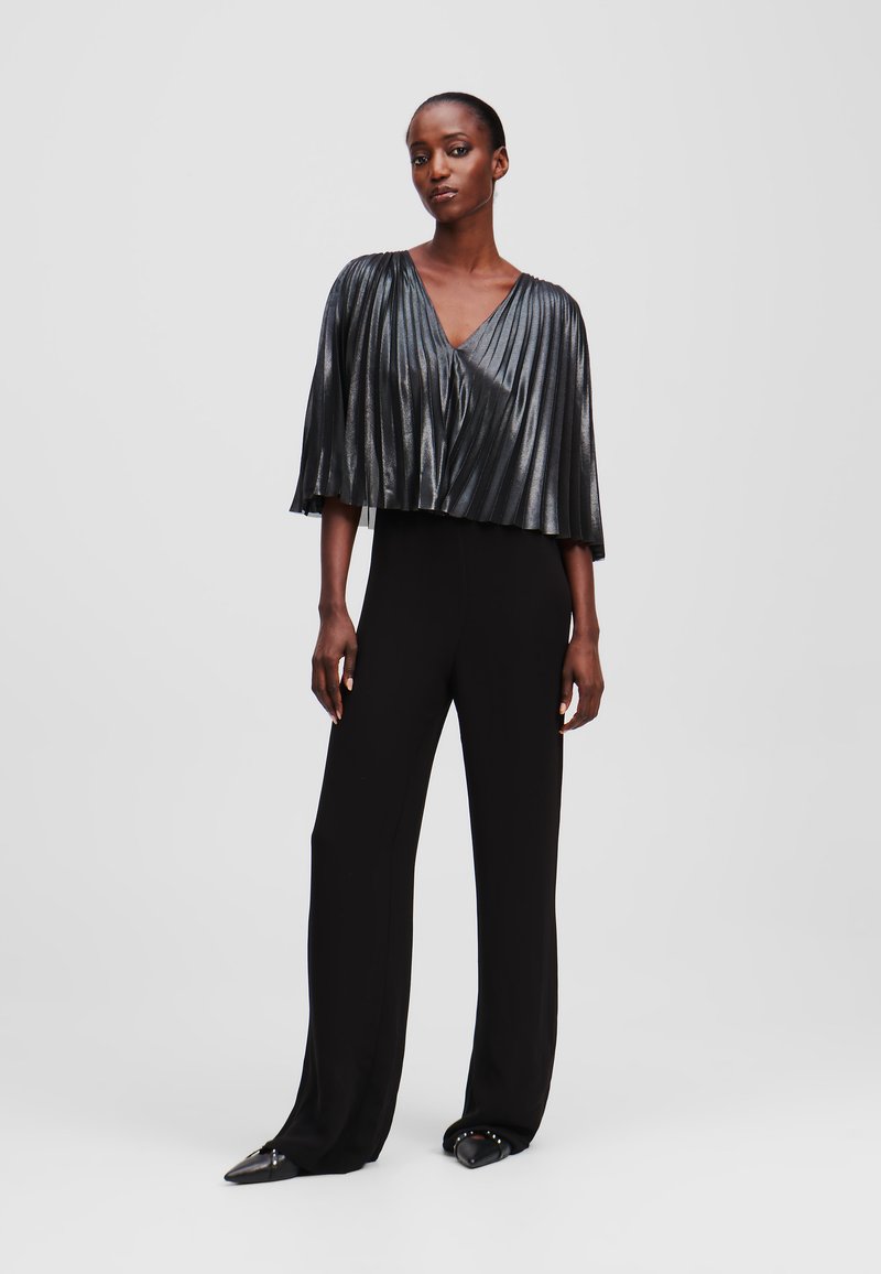 Black jumpsuit with a metallic, pleated short cape, featuring a deep V-neckline and wide legs. Textured material with a glossy finish.