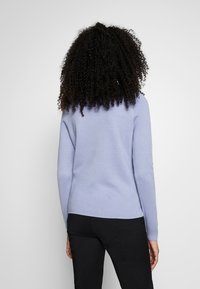 Ljuslila tröja med långa ärmar, rundad halsringning och en mjuk textur. Baksidan har en slät yta och en något kurvad nederkant.