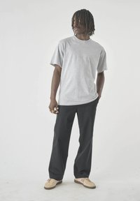 Graues Baumwoll-T-Shirt mit kurzen Ärmeln, kombiniert mit schwarzen Hosen und beigen Schuhen. Das Outfit zeichnet sich durch eine lockere Passform und ein einfaches Design aus.